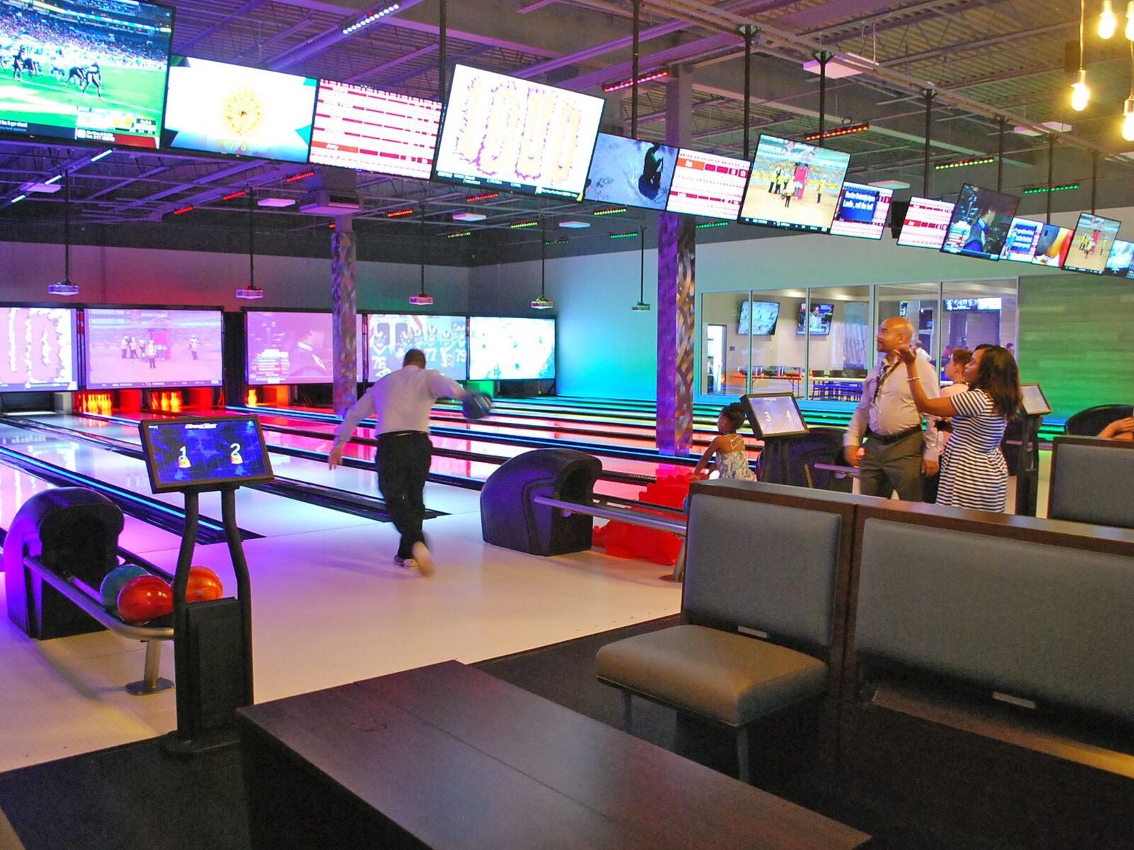 A bowler on the lanes at GameTime Daytona, with the scoring screens and a row of sports screens overhead