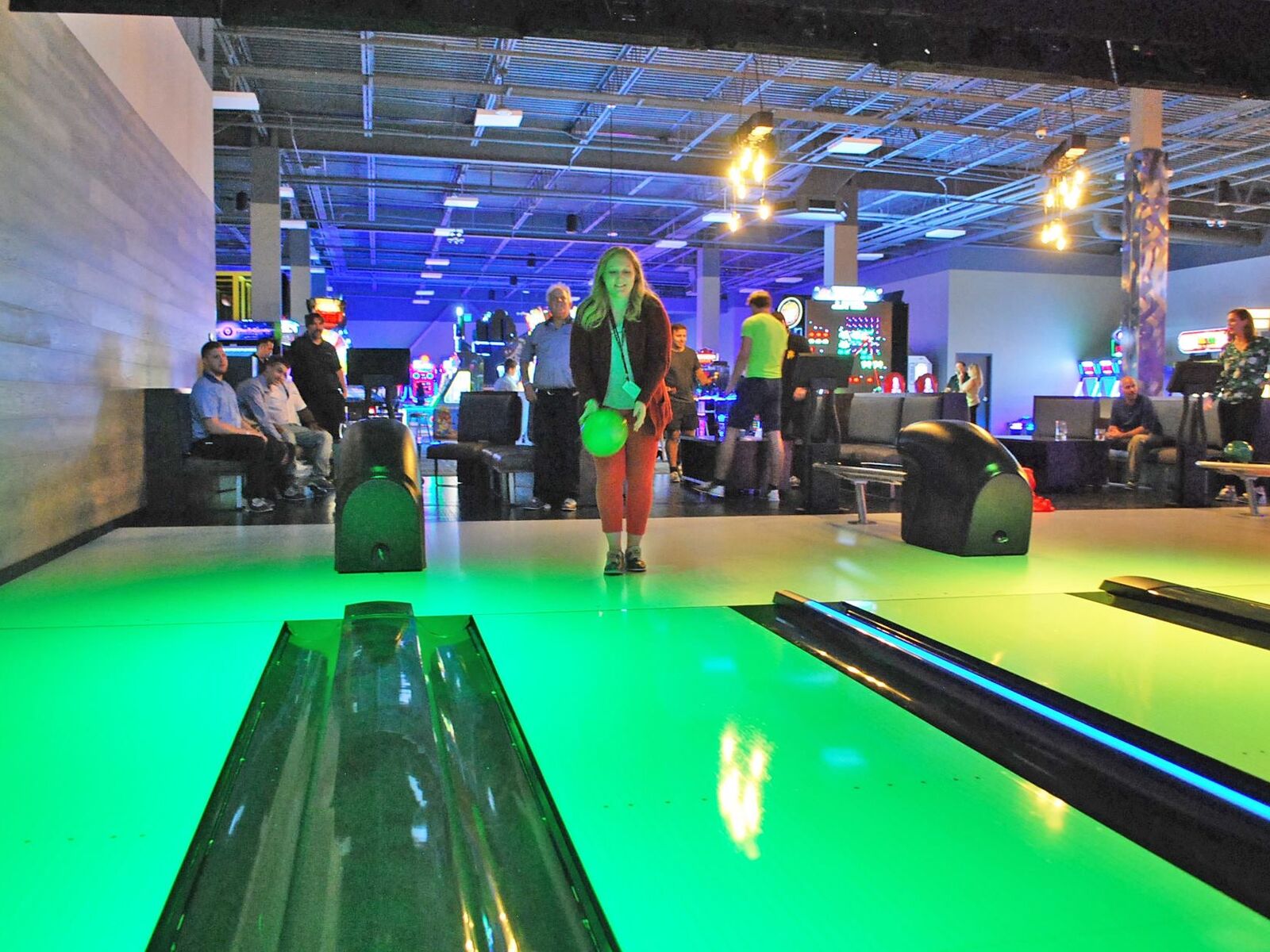 Guests bowling under green light at GameTime Daytona, with the arcade lit purple beyond the lanes