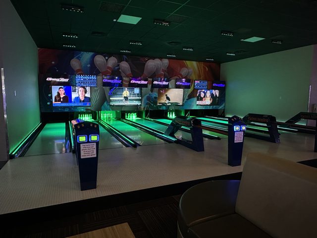 The mini bowling lanes at GameTime Kissimmee, lit green, with the screens above them