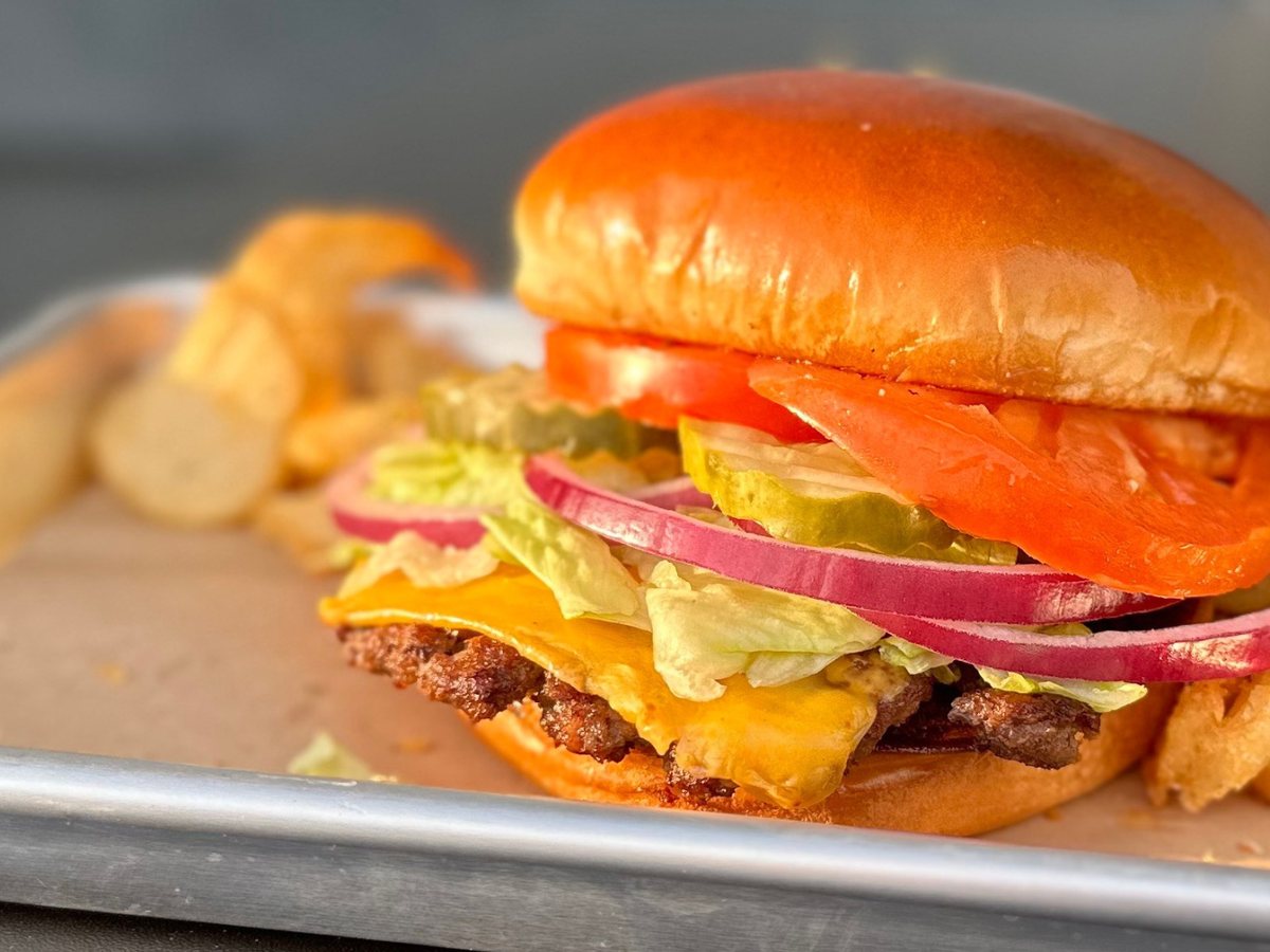 A Classic American Smash Burger with cheese, lettuce, tomato, onion and pickles, fries on the side