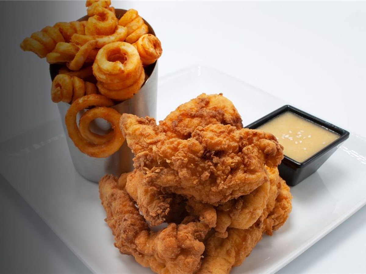 Chicken tenders with a dipping sauce and a cup of curly fries and onion rings