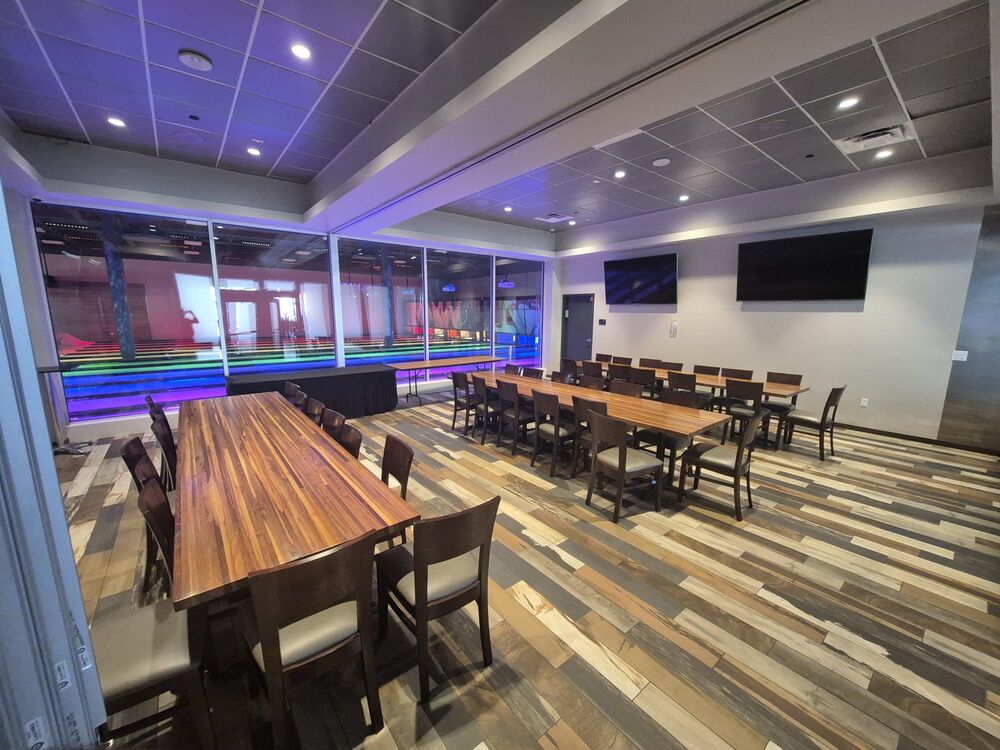 The party space at GameTime Daytona: long wood tables with dark chairs on a plank floor, with a window wall looking out over the lit game floor