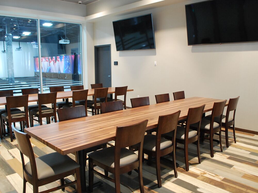 A long wood party table with chairs down both sides at GameTime Daytona, under two wall screens
