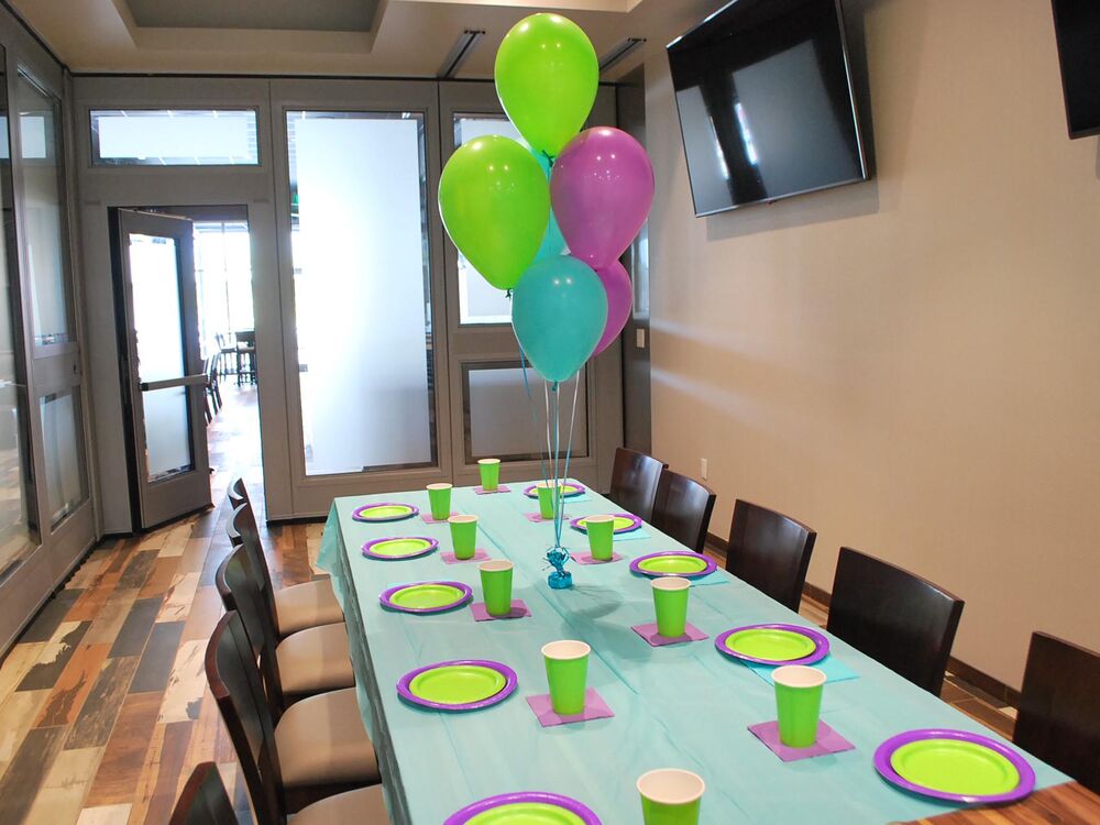 A party table at GameTime Daytona set with a teal cloth, green plates and cups, and a bunch of green, blue and purple balloons