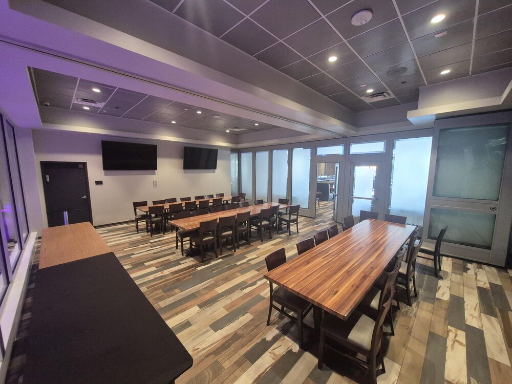 The party space at GameTime Daytona from its doorway: long tables, a screen on the wall and glass doors to the game floor