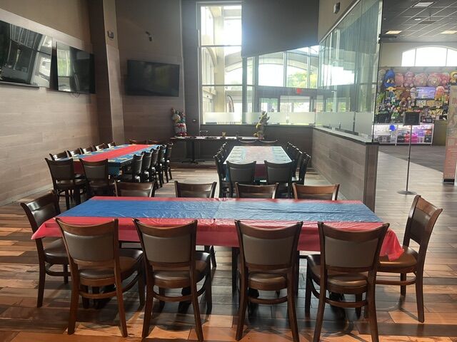 Party tables set with red and blue cloths beside tall windows at GameTime Fort Myers, with a screen on the wall