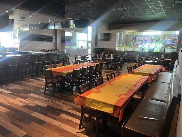 Long tables set with orange and yellow cloths in the restaurant at GameTime Fort Myers, under a row of screens