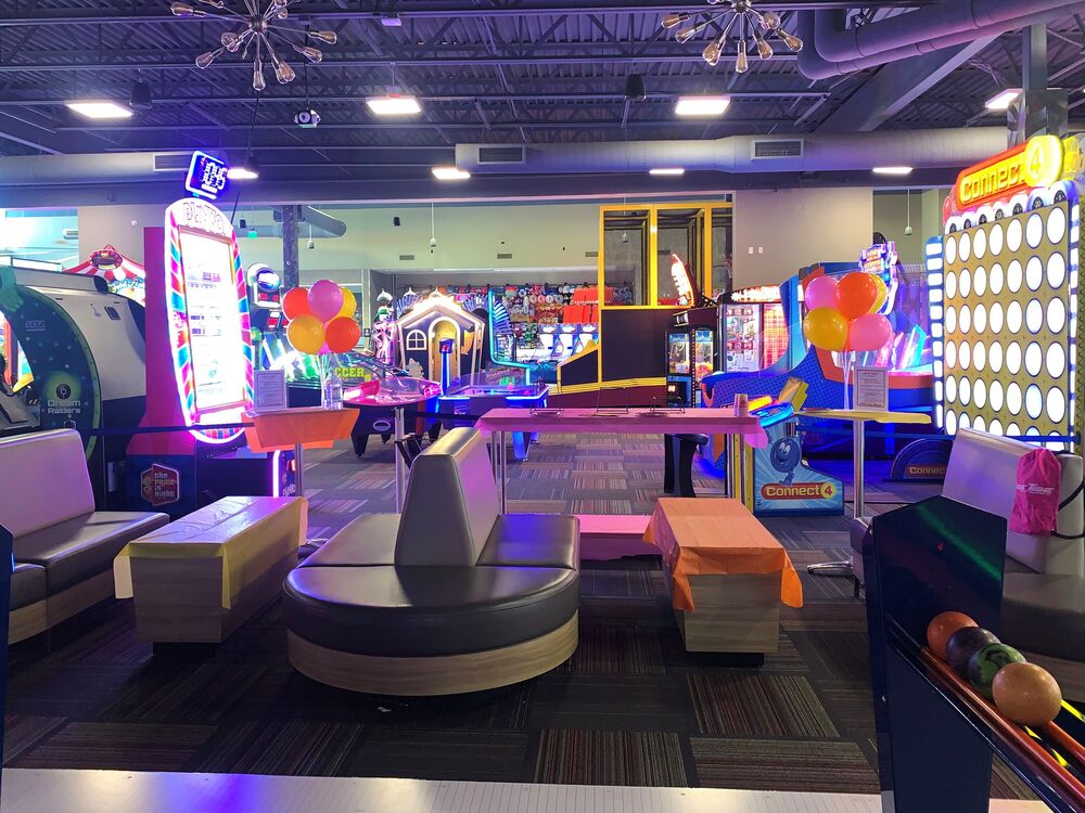 The mini bowling lanes at GameTime Kissimmee with round lounge seating and balloons set out for a party, lit arcade games behind